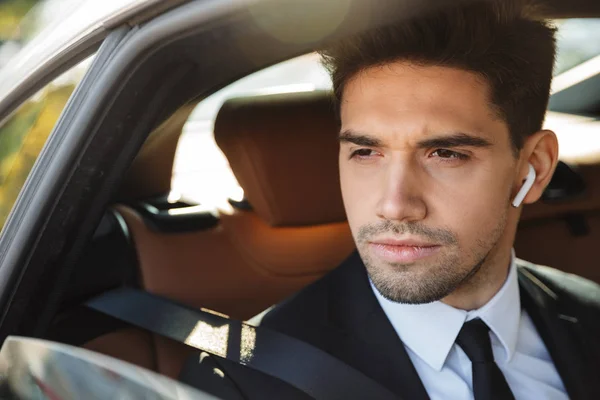 Image of young caucasian businesslike man in suit riding in car — Stockfoto