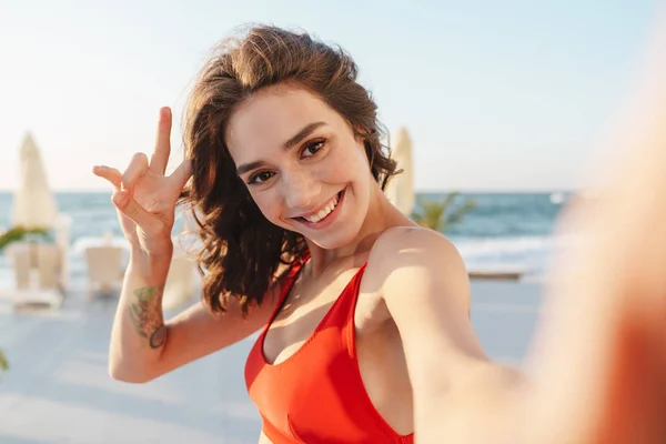 Fotografie usmívající se pěkné ženy gestikulující mírové znamení a brát selfie — Stock fotografie