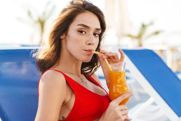 Foto de jovem mulher calma beber suco enquanto sentado na cadeira de gramado — Fotografia de Stock