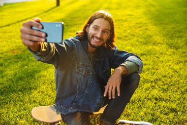 Yakışıklı, gülümseyen genç adam parkta vakit geçiriyor.
