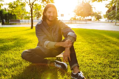 Yakışıklı, gülümseyen genç adam parkta vakit geçiriyor.