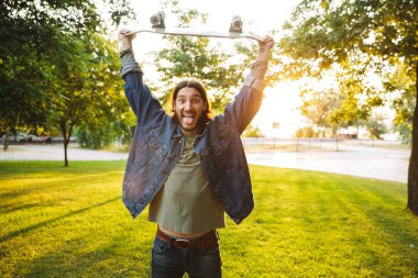 Yakışıklı, gülümseyen genç adam parkta vakit geçiriyor.