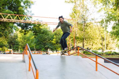 Yakışıklı genç hippi kaykay rampasında kayıyor.