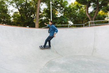 Yakışıklı genç hippi kaykay rampasında kayıyor.