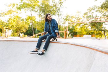 Çekici genç hippi kaykay rampasında oturuyor.