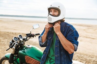 Man biker on his bike outdoors on a beach in a helmet.