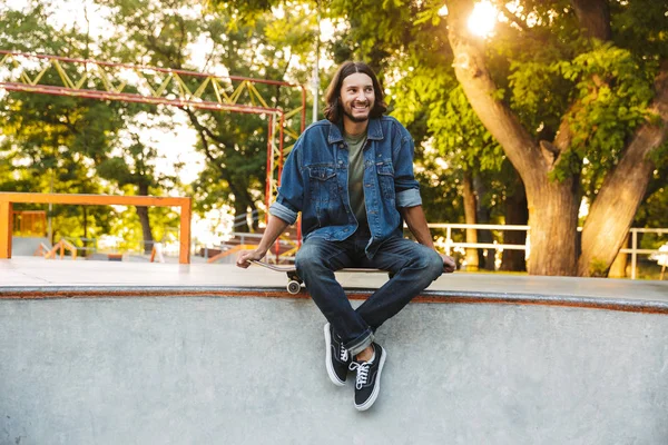 Attractive young hipster man sitting at the skate ramp — Stock Photo, Image