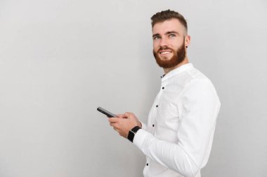 Sakallı mutlu bir adamın cep telefonunda gülümseyip daktilo yazması.