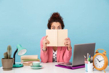 Kitap tutan ve çalışırken kameraya bakan şaşırmış bir kadın resmi