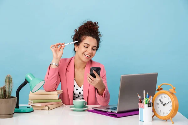 Immagine di una donna bruna che ride usando il cellulare mentre lavora alla scrivania — Foto Stock