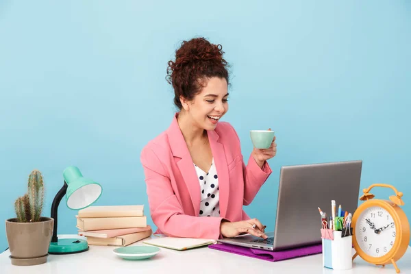 Immagine di una donna sorridente che usa il computer portatile e beve caffè mentre lavora — Foto Stock