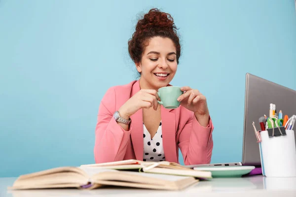 Imagen de la joven feliz bebiendo café y sonriendo mientras trabaja — Foto de Stock