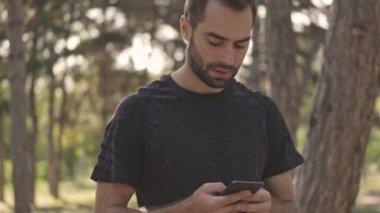 Düşünceli yakışıklı sporcu dışarıda akıllı telefon kullanırken bir şeyler düşünüyor ve etrafa bakıyor.