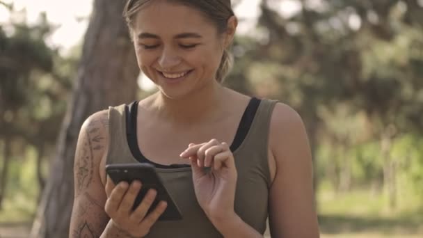 Ευτυχισμένη Νεαρή Όμορφη Αθλητική Γυναίκα Χρησιμοποιώντας Smartphone Στο Πάρκο Εξωτερικούς — Αρχείο Βίντεο