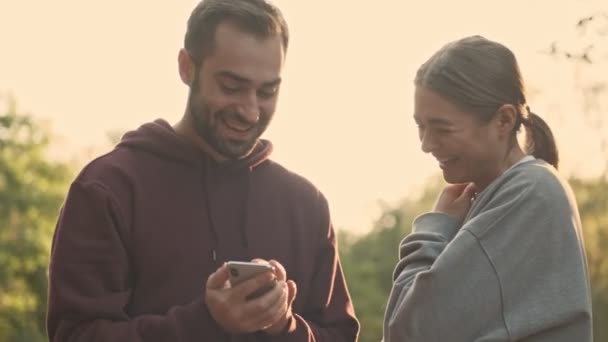 Jovens Felizes Casal Bonito Navegando Fotos Smartphone Divertindo Parque Livre — Vídeo de Stock