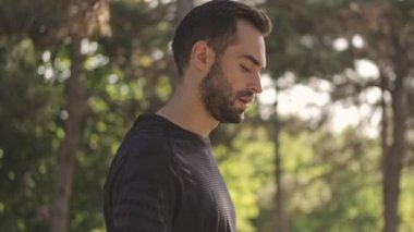 Parkta akıllı telefon kullanırken yürüyen ve etrafa bakan dalgın, güler yüzlü yakışıklı sporcunun yan görüntüsü