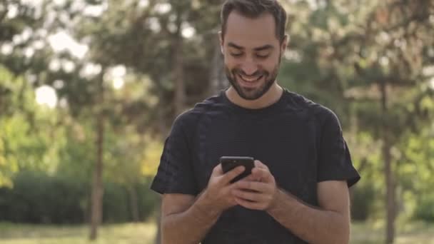 Счастливый Красивый Спортсмен Пишет Сообщение Смартфоне Парке Открытом Воздухе — стоковое видео