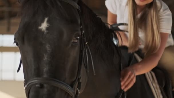 Закрывая Глаза Улыбающаяся Девушка Поглаживает Лошадь Сидя Ней Крытой Конюшне — стоковое видео