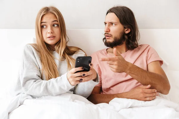 Beautiful confused young couple sitting in bed at home