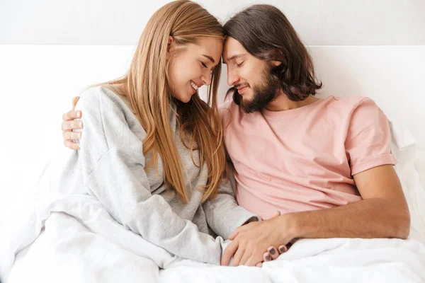 Bonito sorriso jovem casal deitado na cama em casa — Fotografia de Stock