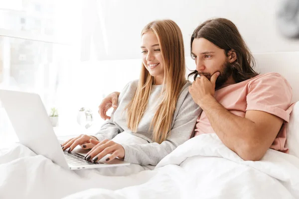 Loving couple in bed using laptop computer at home.