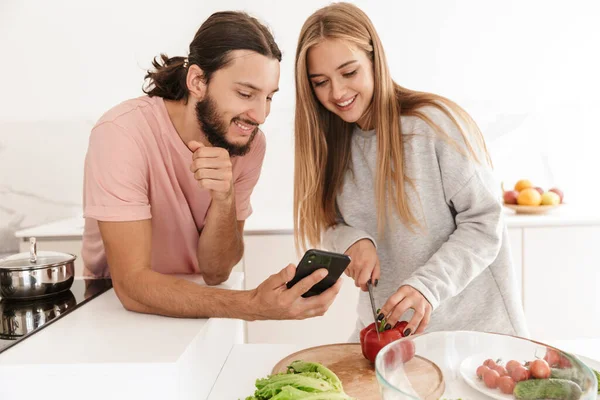 Loving couple at the kitchen using mobile phone — Stock Photo, Image