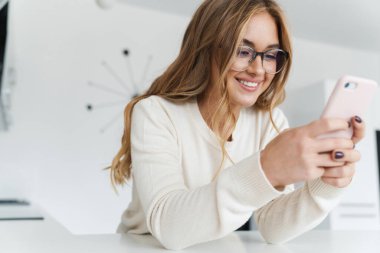 Genç mutlu bir kadının cep telefonuyla yazarken ve gülümserken fotoğrafı.