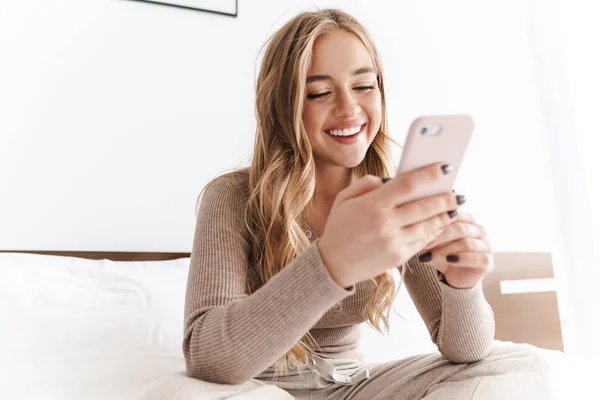 Foto de la joven mujer feliz sonriendo y usando el teléfono celular mientras está sentada — Foto de Stock