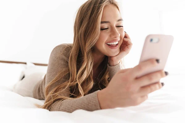 Foto de la joven mujer feliz sonriendo y usando el teléfono celular mientras miente —  Fotos de Stock