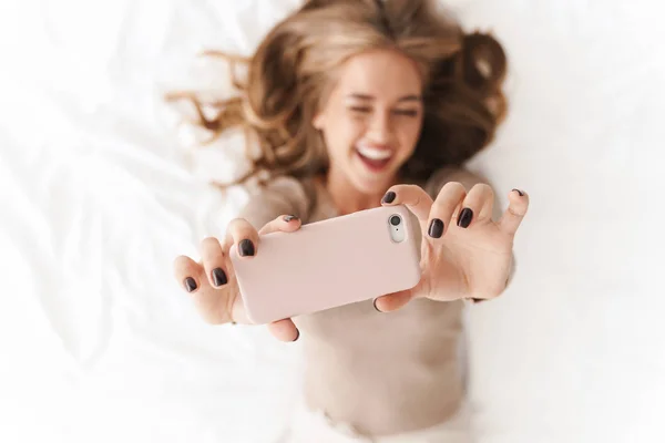 Фото молодой улыбающейся женщины, делающей селфи по мобильному телефону и подмигивающей — стоковое фото