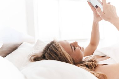 Kafkasyalı neşeli bir kadının yalan söylerken gülümseyip cep telefonu kullandığı fotoğraf.