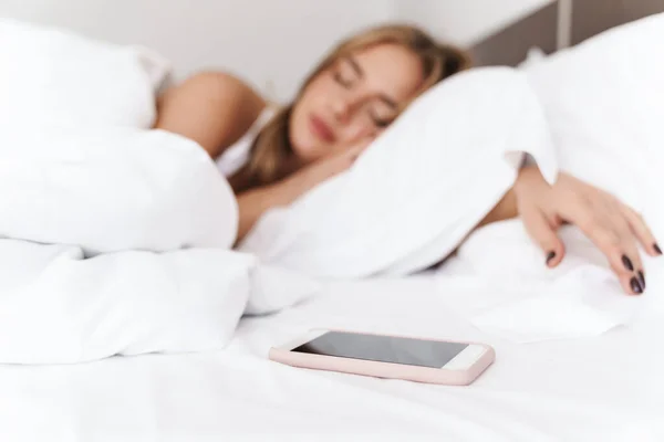 Foto de una joven mujer caucásica durmiendo con un smartphone mientras está acostada —  Fotos de Stock