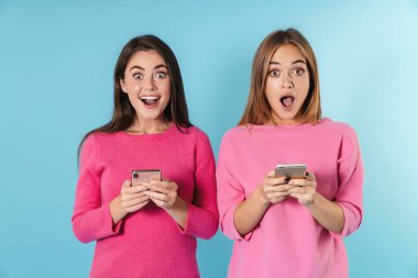 Cep telefonlarıyla yazı yazan ve gülümseyen güzel kadınların fotoğrafı.