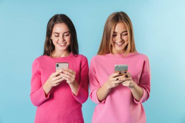 Cep telefonlarıyla yazan ve gülümseyen neşeli kadınların fotoğrafı.