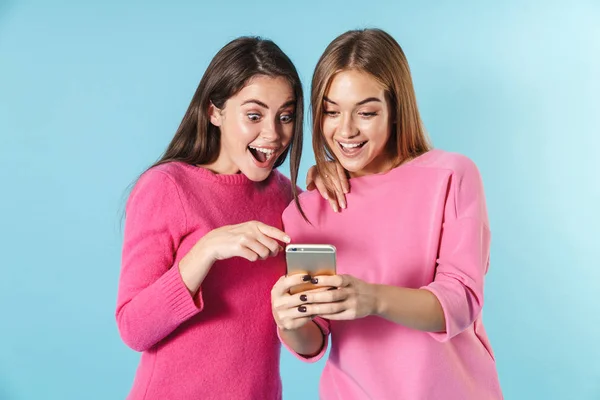 Фото удивленных молодых женщин, использующих и указывающих пальцем на сотовый телефон — стоковое фото
