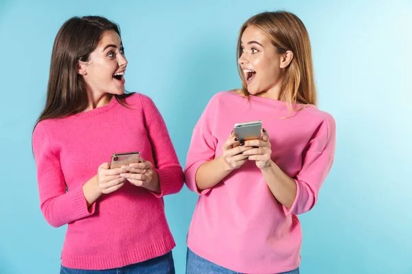 Foto de mulheres jovens surpresas digitando em celulares e sorrindo — Fotografia de Stock