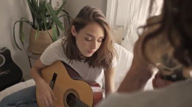 Gülümseyen güzel bir kadın gitar çalarken erkek arkadaşı evde retro kamera ile video çekiyor.
