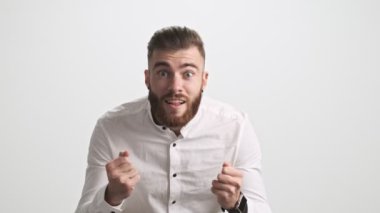 Çekici sakallı bir adam bir şey izlerken tezahürat yapıyor sonra beyaz duvar arkasında hayal kırıklığı yaşıyor.