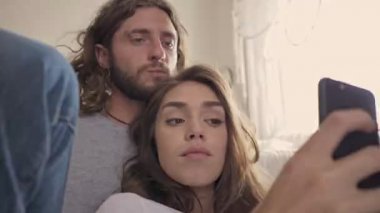 Evdeki yatağın yanında otururken akıllı telefondan selfie çeken komik çiftin yakın görüntüsü.