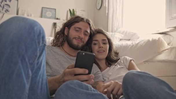 Alegre Casal Lindo Usando Smartphone Enquanto Sentados Juntos Perto Cama — Vídeo de Stock