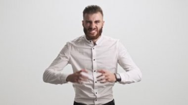Çekici sakallı bir adam, beyaz duvar arkasına izole edilmiş ellerini kameraya kaldırarak çığlık atıyor.
