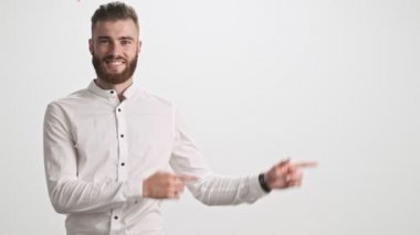 Beyaz gömlek giyen genç, pozitif sakallı bir adam iki eli de beyaz duvar arkasında izole bir şekilde kenarı gösteriyor.