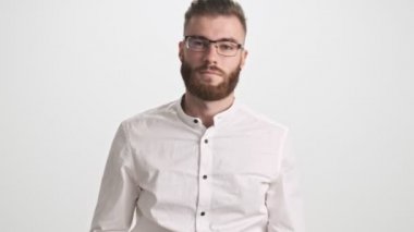 Beyaz gömlek ve gözlük takan genç sakallı bir adam, parmağı beyaz duvar arkasında izole bir şekilde hareket ediyor.