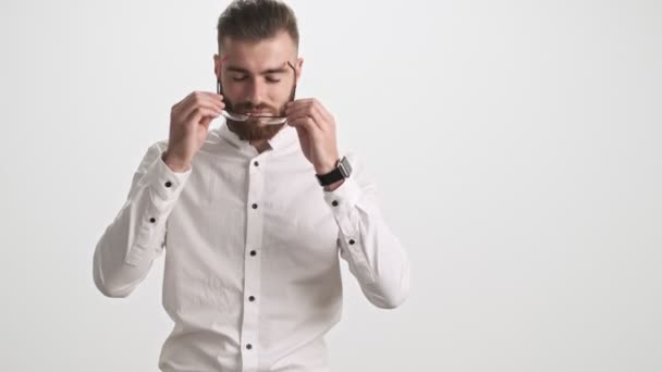 Jovem Barbudo Positivo Vestindo Uma Camisa Branca Coloca Óculos Isolados — Vídeo de Stock