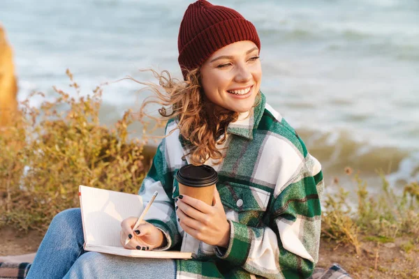 Imagen de una mujer sonriente tomando café y tomando notas en el diario — Foto de Stock