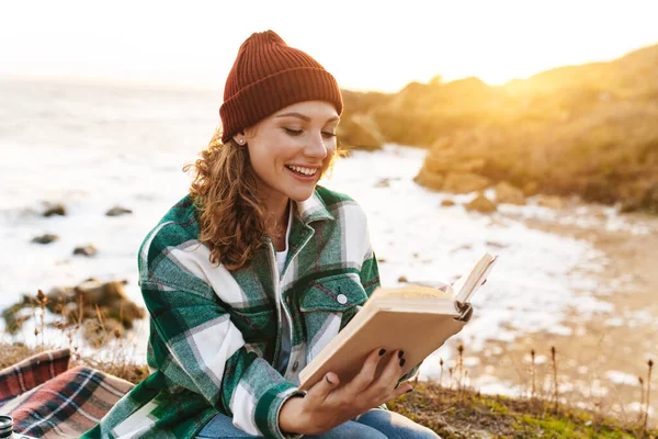 Bild einer kaukasischen fröhlichen Frau, die Buch liest und im Sitzen lächelt — Stockfoto