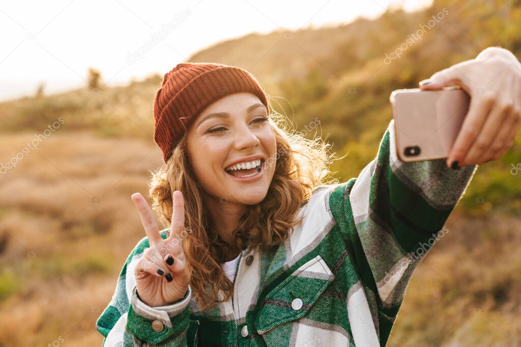 Image of woman taking selfie photo on cellphone while walking ou
