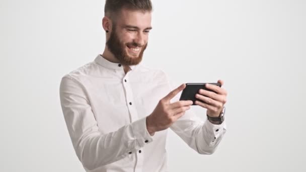 셔츠를 매력적 턱수염 남자가 수평으로 고립된 스마트폰으로 무엇인가를보고 — 비디오