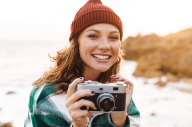 Genç bir kadının yürürken retro kamerada fotoğraf çekmesi 