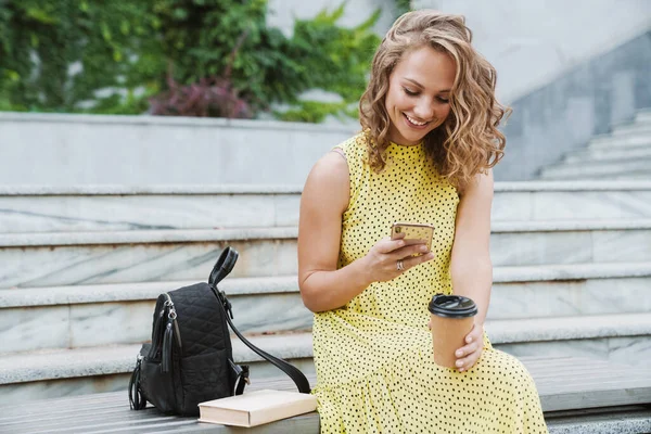 Femme assise à l'extérieur à boire du café à l'aide d'un téléphone mobile . — Photo